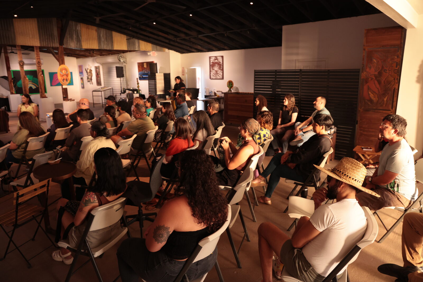 A full room of community members seated for a conversation in a local art space